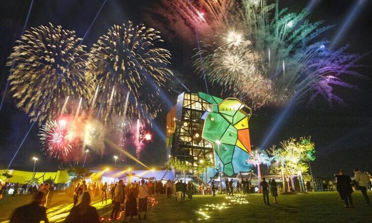 Crowds gather at night under vibrant fireworks during the SeaFire 2025 festival, one of the major Surfers Paradise events held near a colorful modern building on the beachfront.